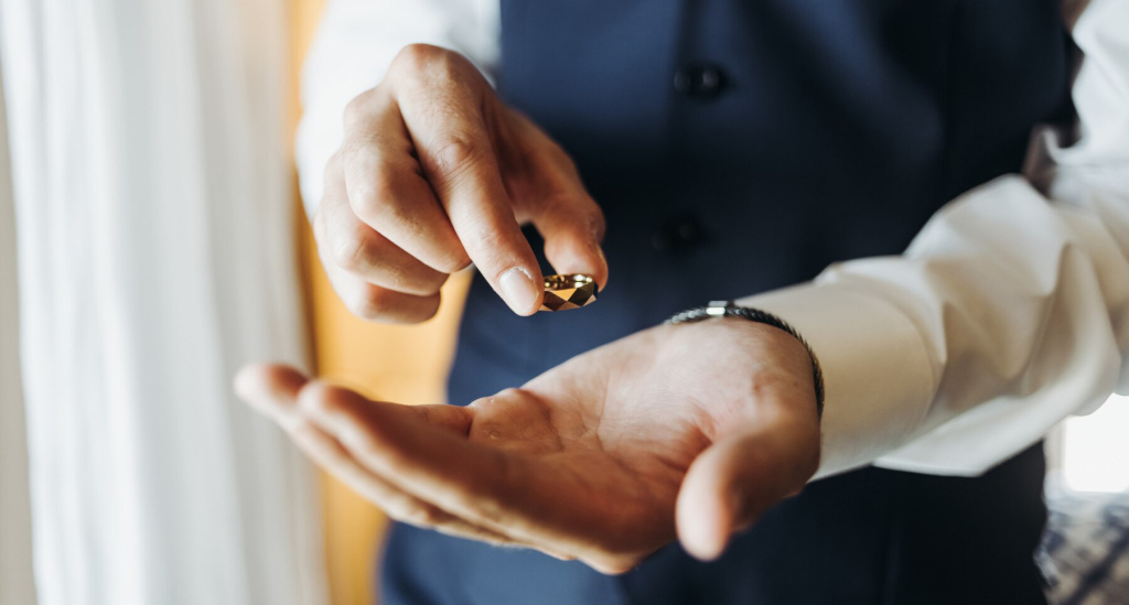 groom-holds-wedding-ring-standing-before-window-hotel-r_8353-8963.jpg